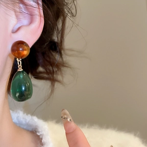 Detail of a green resin teardrop earring with amber bead on a model's ear