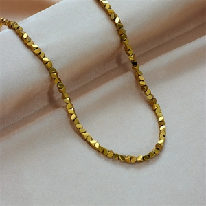 Minimalist gold beaded necklace with faceted geometric charms on champagne silk fabric