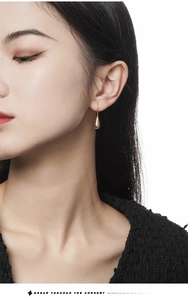 Close-up of elegant gold teardrop earrings worn by a model against a white background