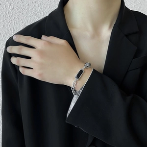 Detail of silver chain bracelet with black stone and skull charm on model's wrist