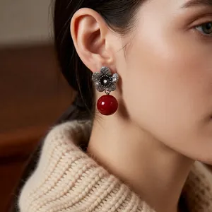 Vintage silver flower earrings with red pearl pendants worn by a model in warm light