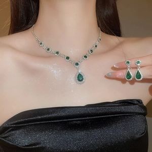 Close-up of sparkling pear-shaped green emerald pendant necklace and matching earrings