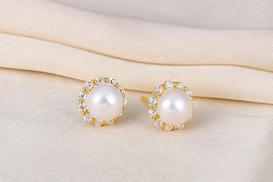 Macro view of white round pearl earrings with gold metal and zircon halo on silk cloth