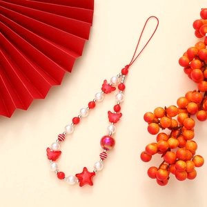 Detail of red and white beaded phone strap with star and butterfly charms on beige base