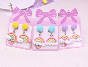 Detailed view of three pairs of rainbow cloud clip-on earrings for kids on pink card