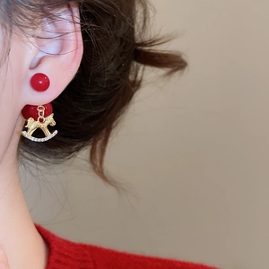 Gros plan de boucles d'oreilles perles rouges et cheval à bascule doré portées par le mannequin