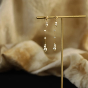 Macro shot of gold shell earrings with long pearl tassels on a T-shaped display stand