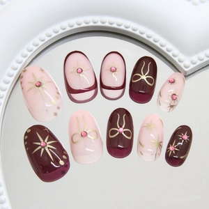 Deep red and pink press-on nails with golden starbursts, bows, and sparkling rhinestones