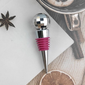 Disco ball wine stopper with pink rubber seal on a rustic tabletop setting
