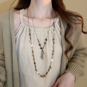 Dettaglio della collana di perline vintage con monete in metallo e lunghe nappe su maglia beige
