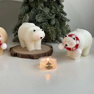 Detail of polar bear candles with red striped scarves and burning tea light on wooden base
