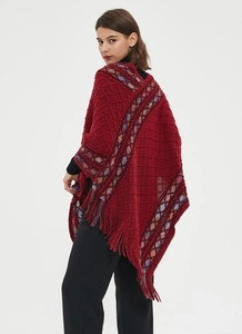 Close-up of deep red knitted poncho featuring diamond texture and stylish tassel edges