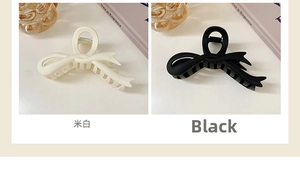 Detail of matte bow hair claws in cream and black showing inner teeth and spring mechanism