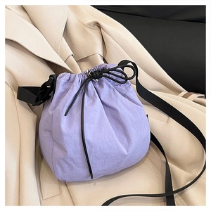 Detail of purple nylon bucket bag with drawstring closure and black strap on beige coat