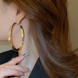 Detailed close-up of thick gold tubular hoop earrings with high-polish mirror finish