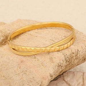 Brazalete cruzado geométrico de acero inoxidable dorado sobre una piedra natural