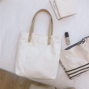 Flat lay of a white canvas tote bag with brown leather handles and a striped shirt