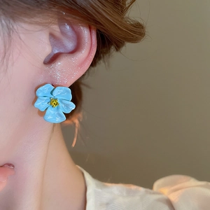 Detail of light blue enamel flower earring with yellow gemstone worn by a model