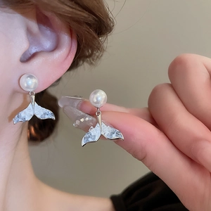 Close-up of silver fish tail pearl earrings worn by a model showing exquisite details