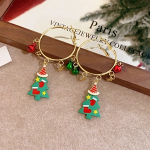 Golden Christmas tree hoop earrings with festive bells and stars on a wooden stand