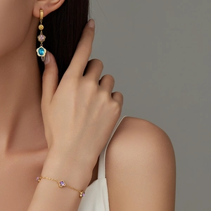 Detail showing gold earrings and bracelet with colorful clover-shaped gemstones