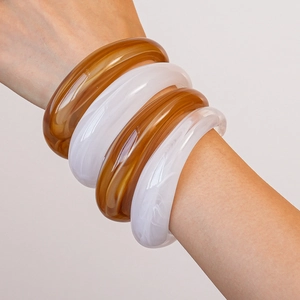 Detail of chunky acrylic bangles in amber and white marble patterns on wrist