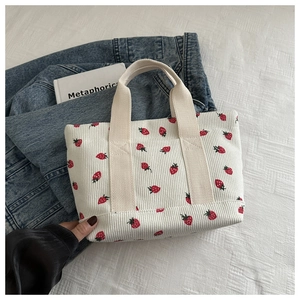 Close-up of white corduroy handbag featuring red strawberry patterns and fabric handles
