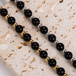 Tiger eye and obsidian beaded bracelet with gold metal spacers on a stone background