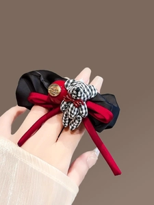 Detail of checkered bear bow scrunchie with red ribbons and gold metal tag