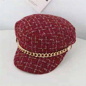 Close-up of red tweed baker boy hat with woven texture and a decorative gold metal chain