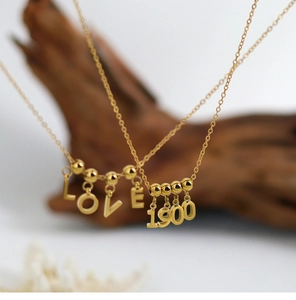 Detail of gold LOVE and 1900 pendants on a fine chain with polished metallic finish