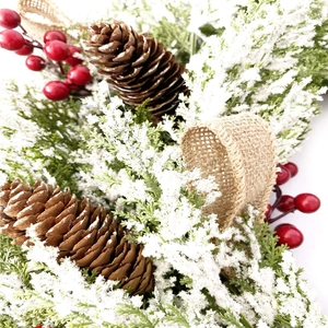 Couronne de Noël avec aiguilles de pin enneigées, cônes bruns et baies rouges sur blanc