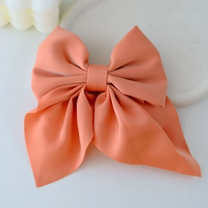 Close-up of a coral pink satin bow hair clip with elegant long ribbons on a tray