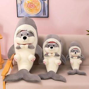 Three sizes of plush shark-costume dog toys displayed on a cozy beige fabric sofa
