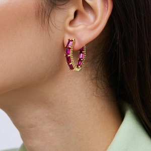 Detail of model wearing gold hoop earrings with fuchsia rectangular zircons