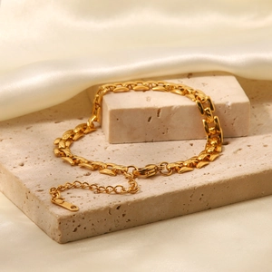 Detail of 18K gold stainless steel chain bracelet on a textured stone with silk fabric