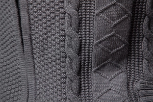 Dettaglio macro del cardigan grigio scuro in maglia a trecce con trame a rombi