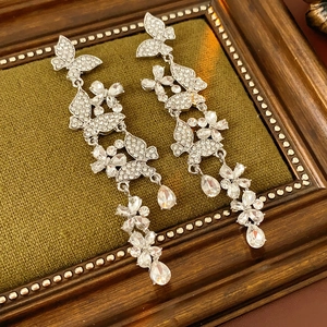 Macro shot of silver butterfly earrings with rhinestones and pear-cut drops on green velvet