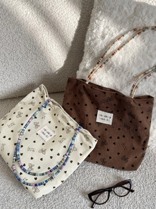 Corduroy tote bags with bow heart prints and colorful beaded handles on soft background