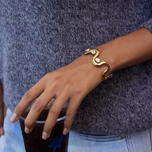 Detail of a wavy gold stainless steel cuff bracelet with white cubic zirconia stones