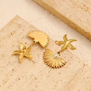 Gold ocean earrings featuring starfish and shell charms with pearl accents on beige stone