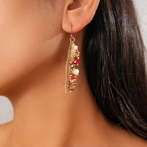 Close-up of bohemian tassel earrings with gold chains and colorful glass beads on a model