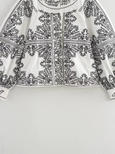 Détail de motifs de broderie noirs complexes sur une veste blanche décontractée à col rond
