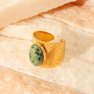 Detailed macro view of wide gold titanium ring with green oval stone on stone slabs