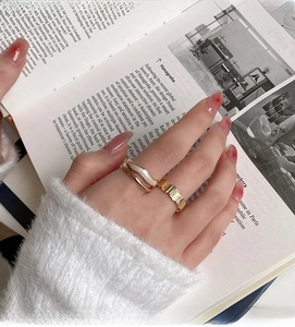 Close-up of golden wavy ring with white enamel and textured band on finger