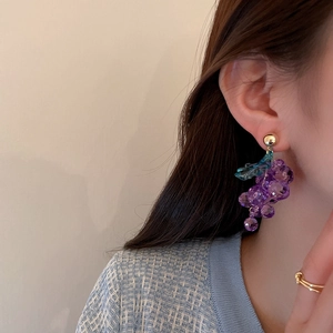 Close-up of purple grape earrings with green leaves and gold hooks on a model