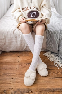 Detailed view of white coral fleece knee high socks and plush slippers in a home setting