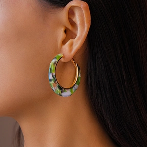 Macro side view of a model wearing the C-shaped marbled acetate hoop earrings with gold metal