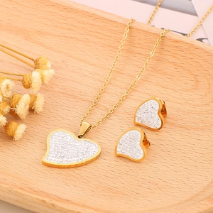 Sparkling gold heart necklace and earrings jewelry set with pavé crystals on a wooden tray