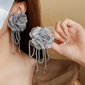 Detail of grey fabric flower earrings with long bead tassels on a model profile